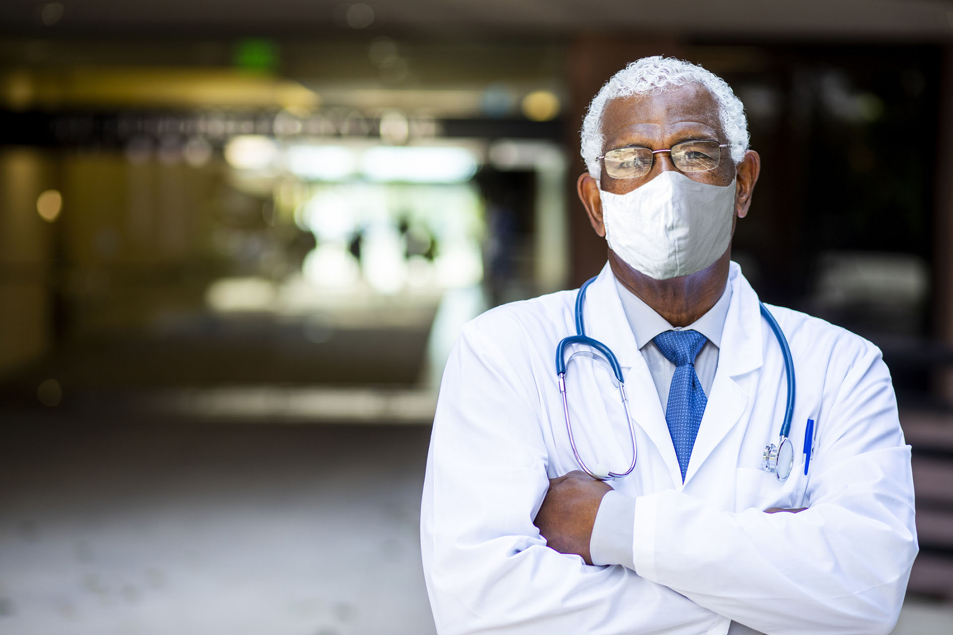 African American Doctor, white hair and mask with white coat and stethoscope around his shoulders